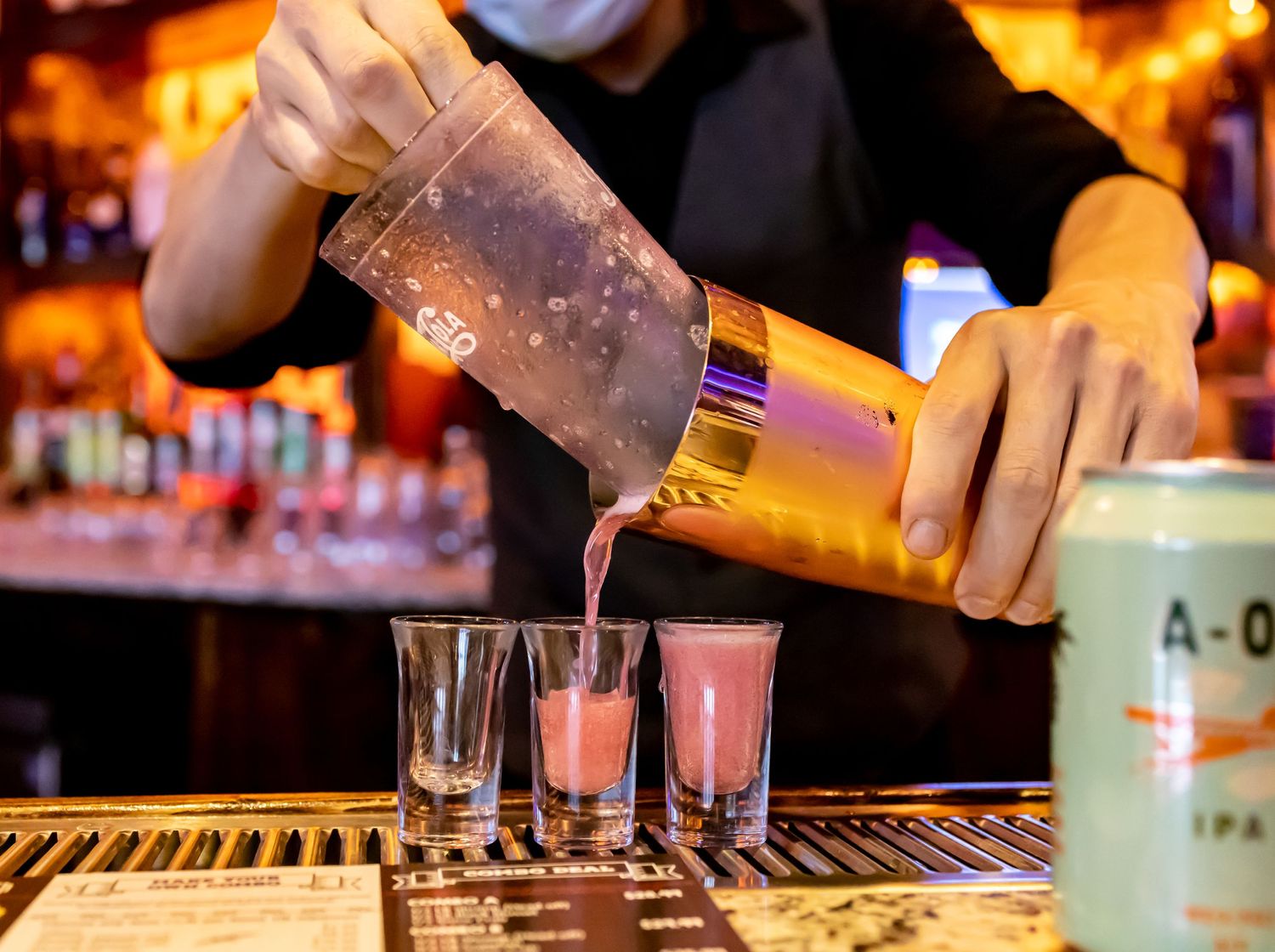 Bartender pouring shots from a shaker into glasses at a dimly lit bar.