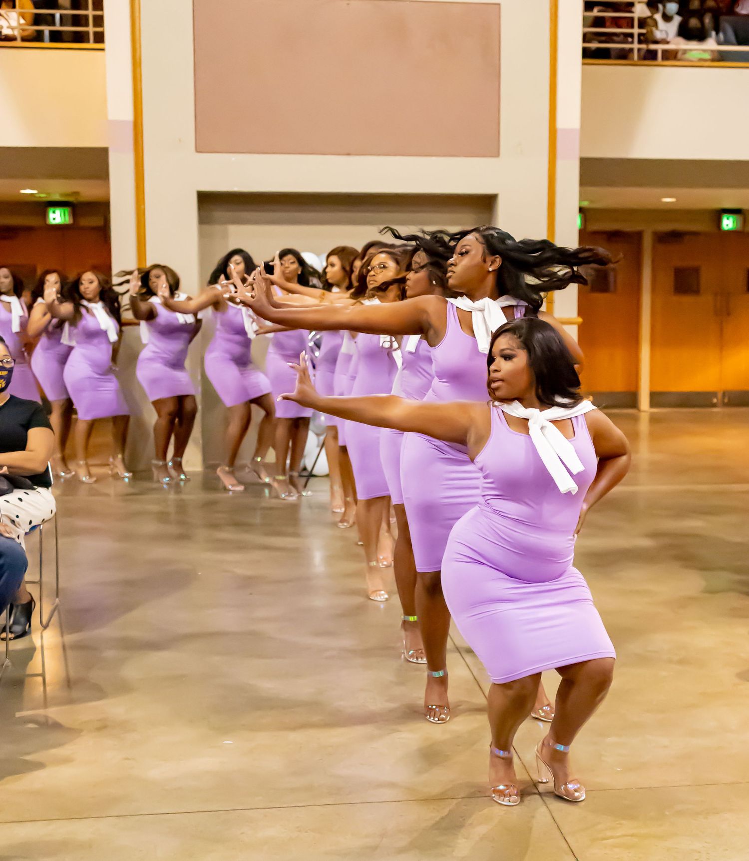 Group of dancers in purple dresses performing choreographed routine in an auditorium.