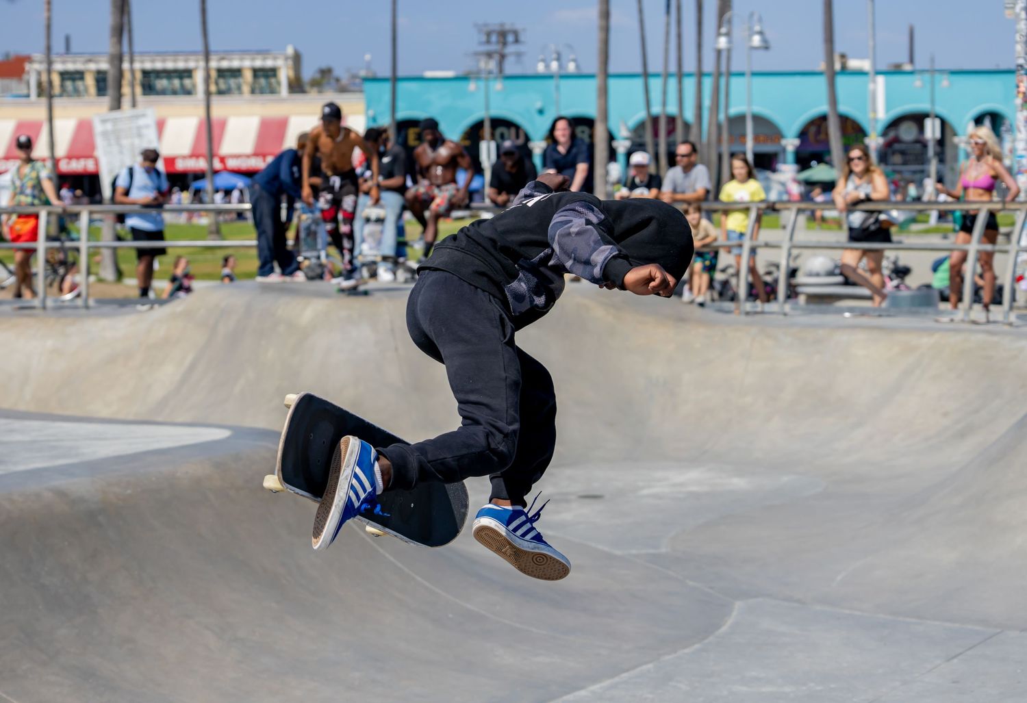 Skateboarder performing aerial trick at outdoor skate park with beach in background.