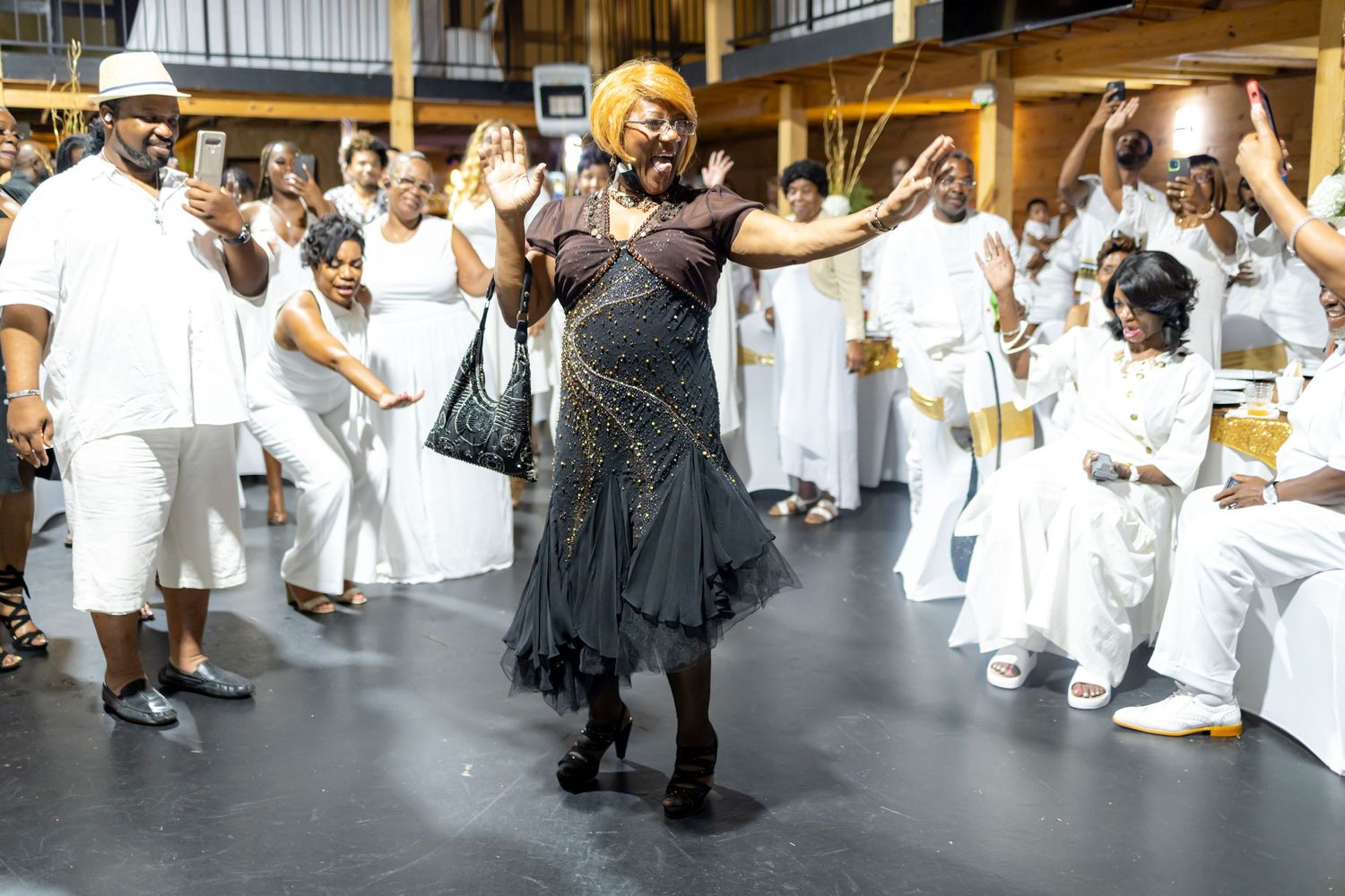 Festive gathering of people in white attire dancing in a large indoor space.