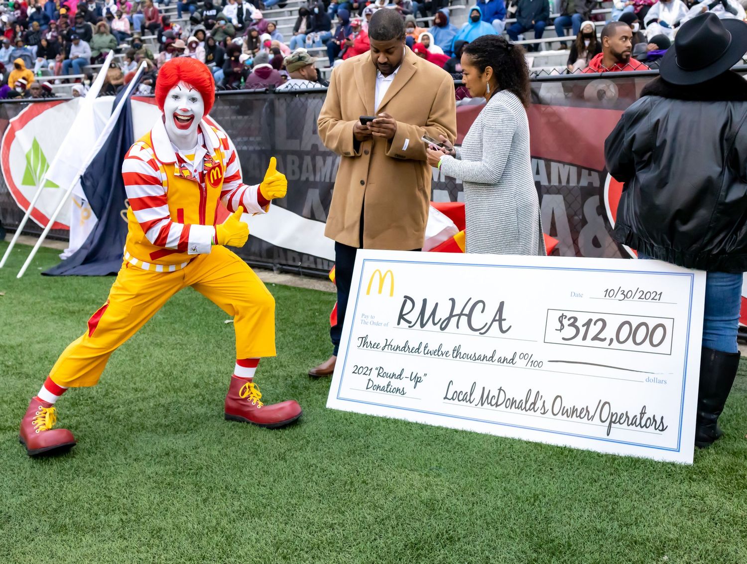 Ronald McDonald mascot presenting large check at a sporting event.