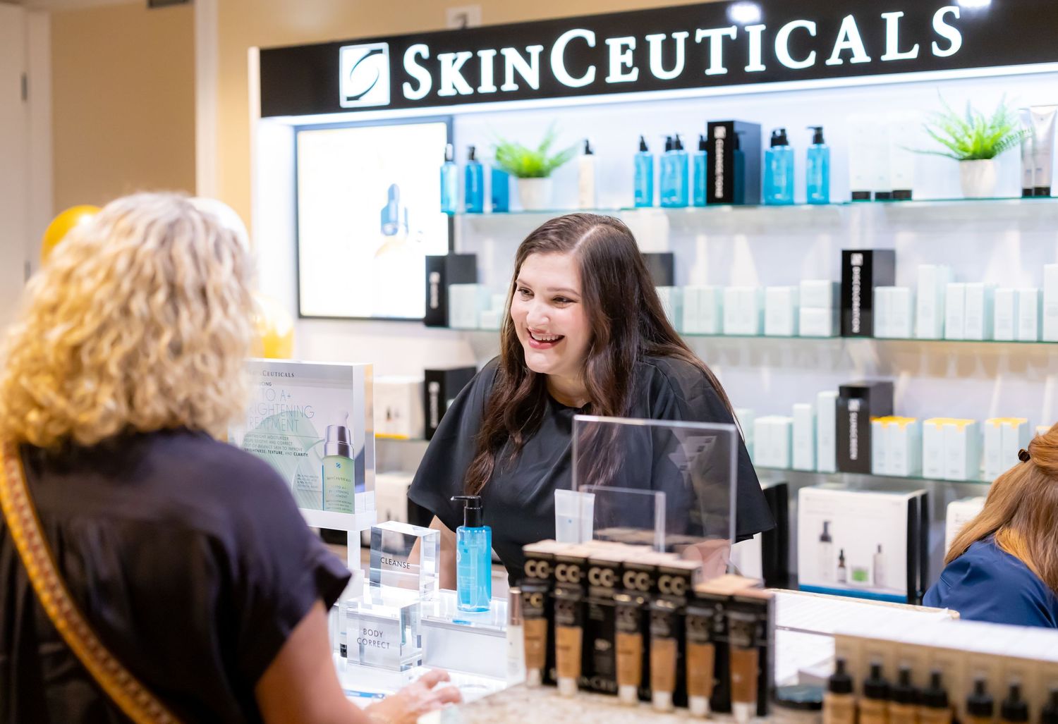 Beauty retail counter displaying SkinCeuticals products with customers being helped by staff.