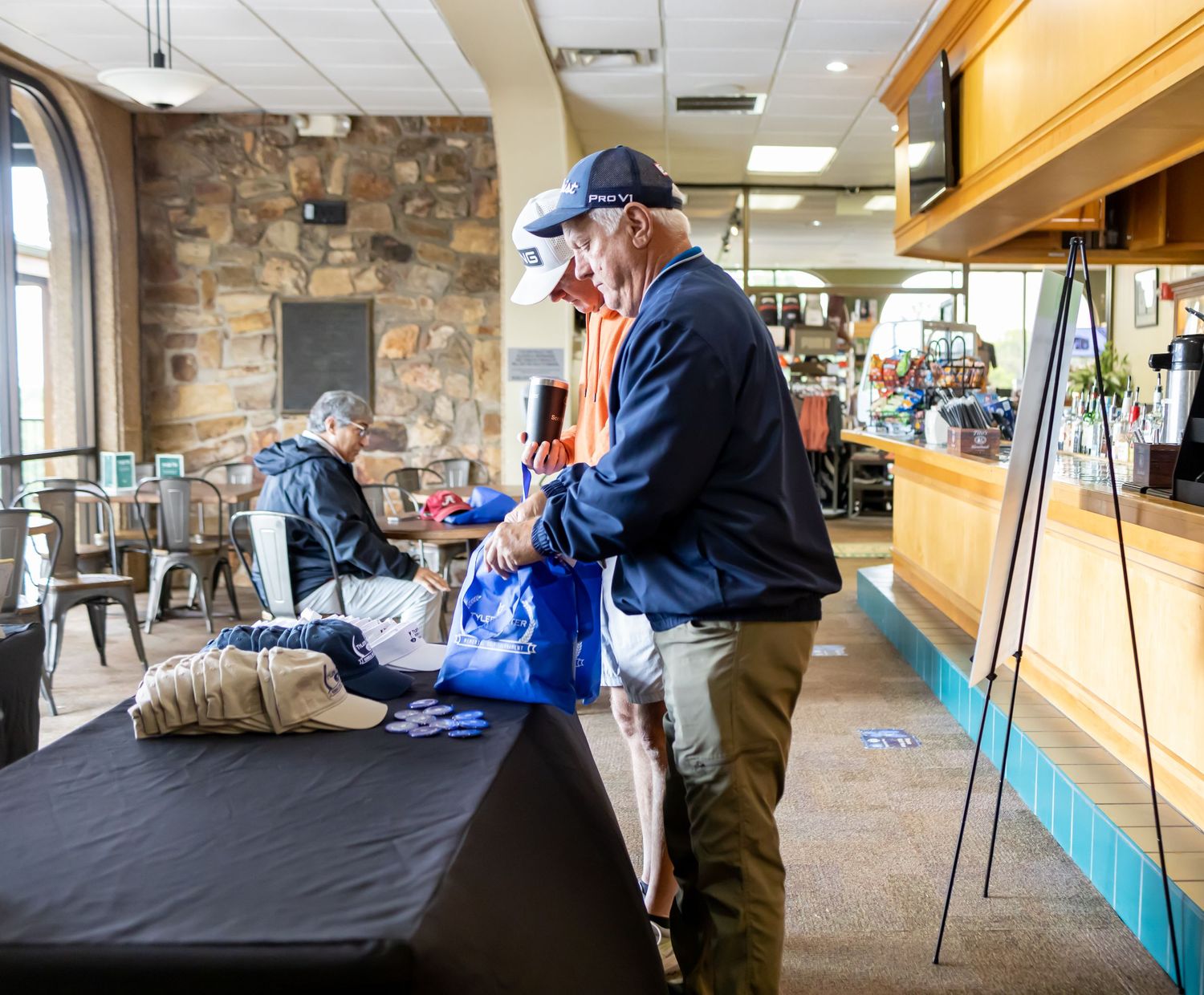 Volunteer sorting through blue bags at registration table with stone wall background.