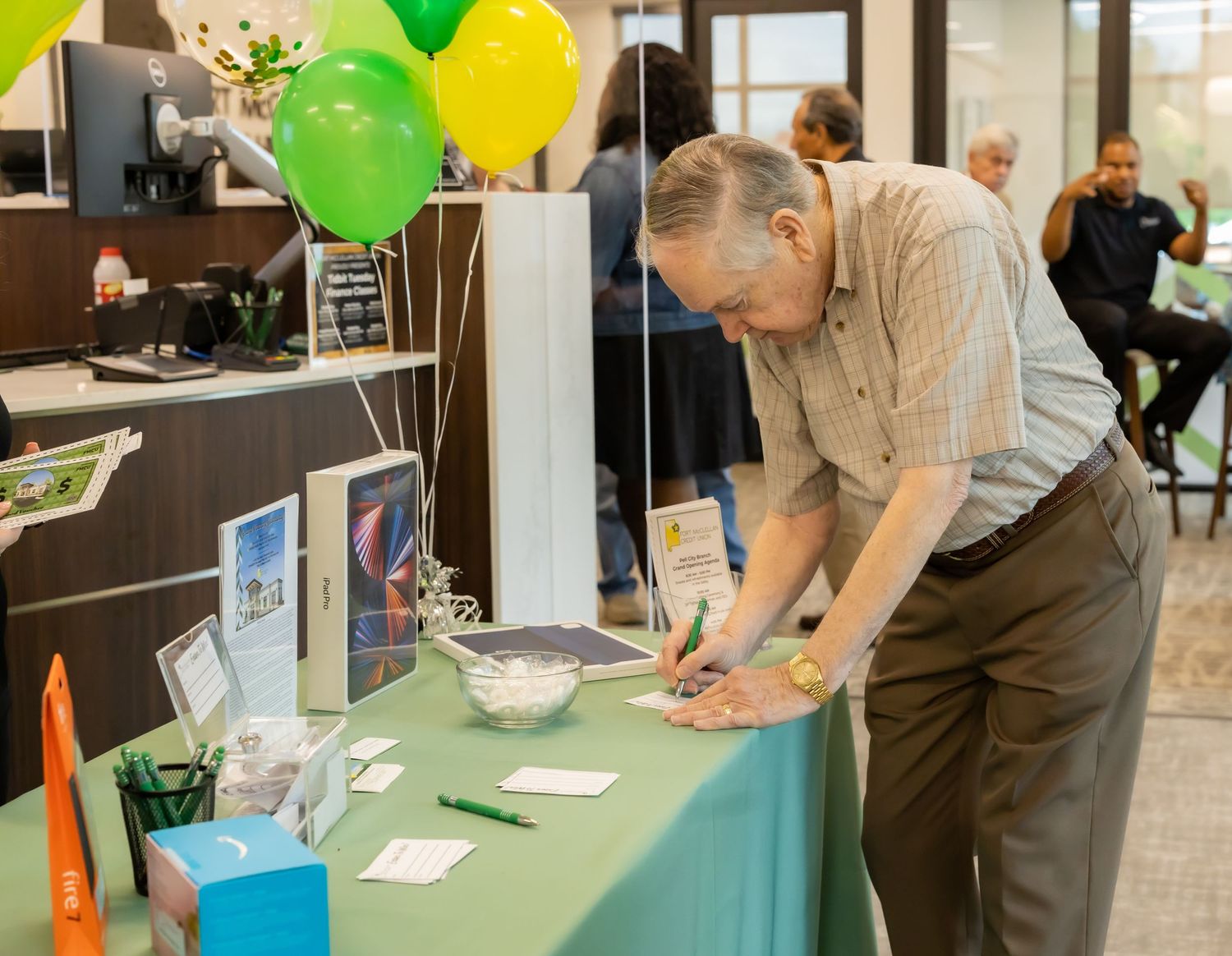Senior attendee fills out form at event registration table decorated with colorful balloons.