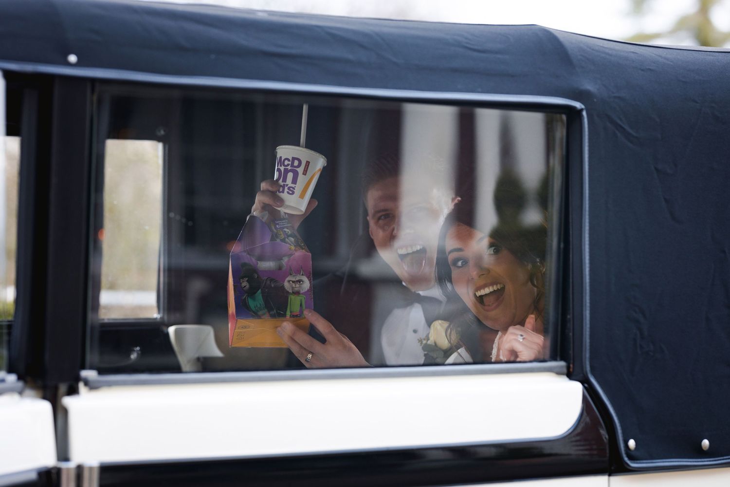 Laughter and celebration inside a vintage car with drinks being held up.