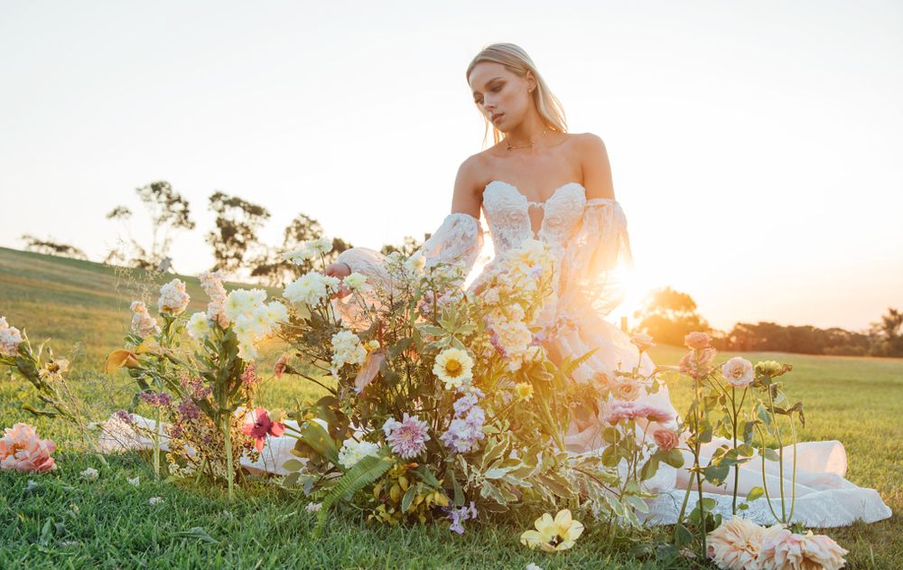 A romantic bridal photo in a white wedding dress surrounded by wildflowers at sunset in a field.