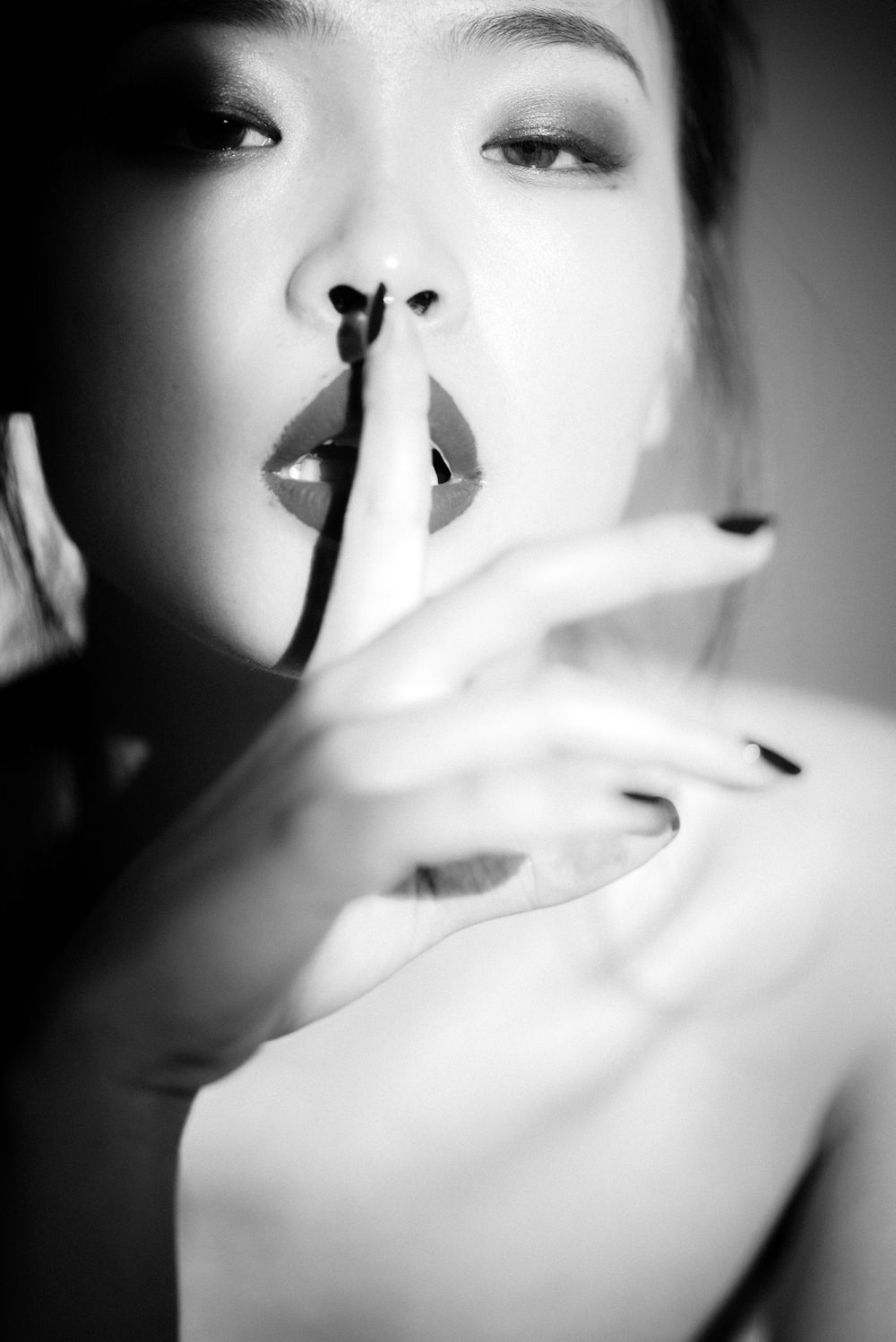 Dramatic black and white portrait with hushing gesture in soft focus.