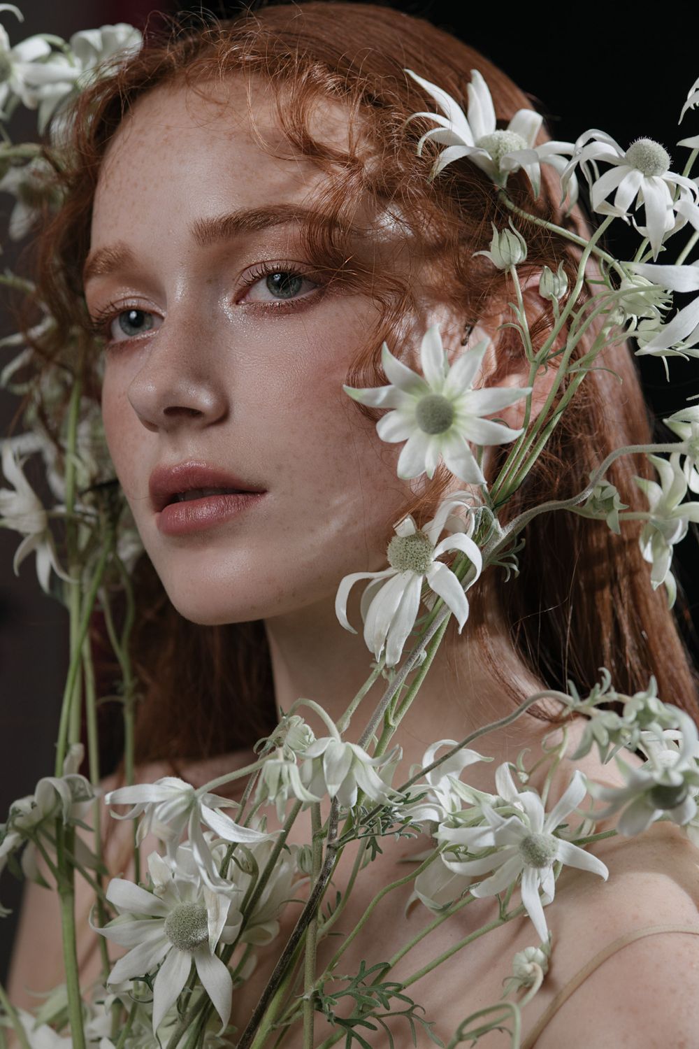 Ethereal portrait with white florals and delicate daisies framing soft natural makeup.