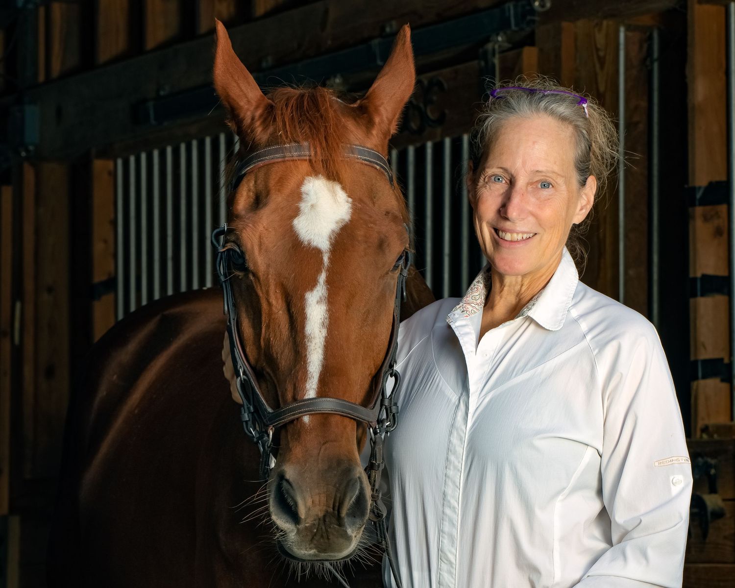Brown horse with white blaze stands next to handler in stable interior.