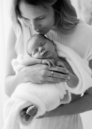 Tender moment captured in black and white as sleeping newborn rests in gentle embrace.