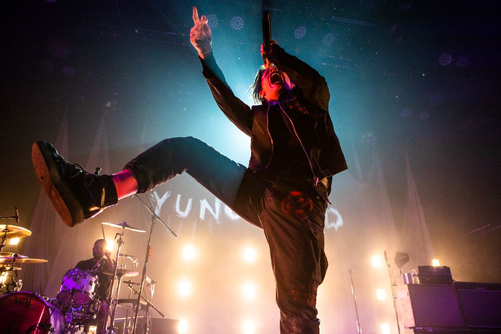 A silhouetted performer jumps energetically on stage during a concert with bright orange and yellow lighting effects. Yungblud