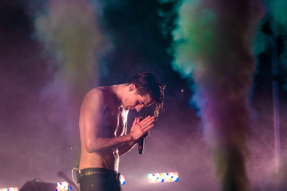 A performer on stage is silhouetted against colorful smoke and dramatic lighting during a concert performance. Geazy