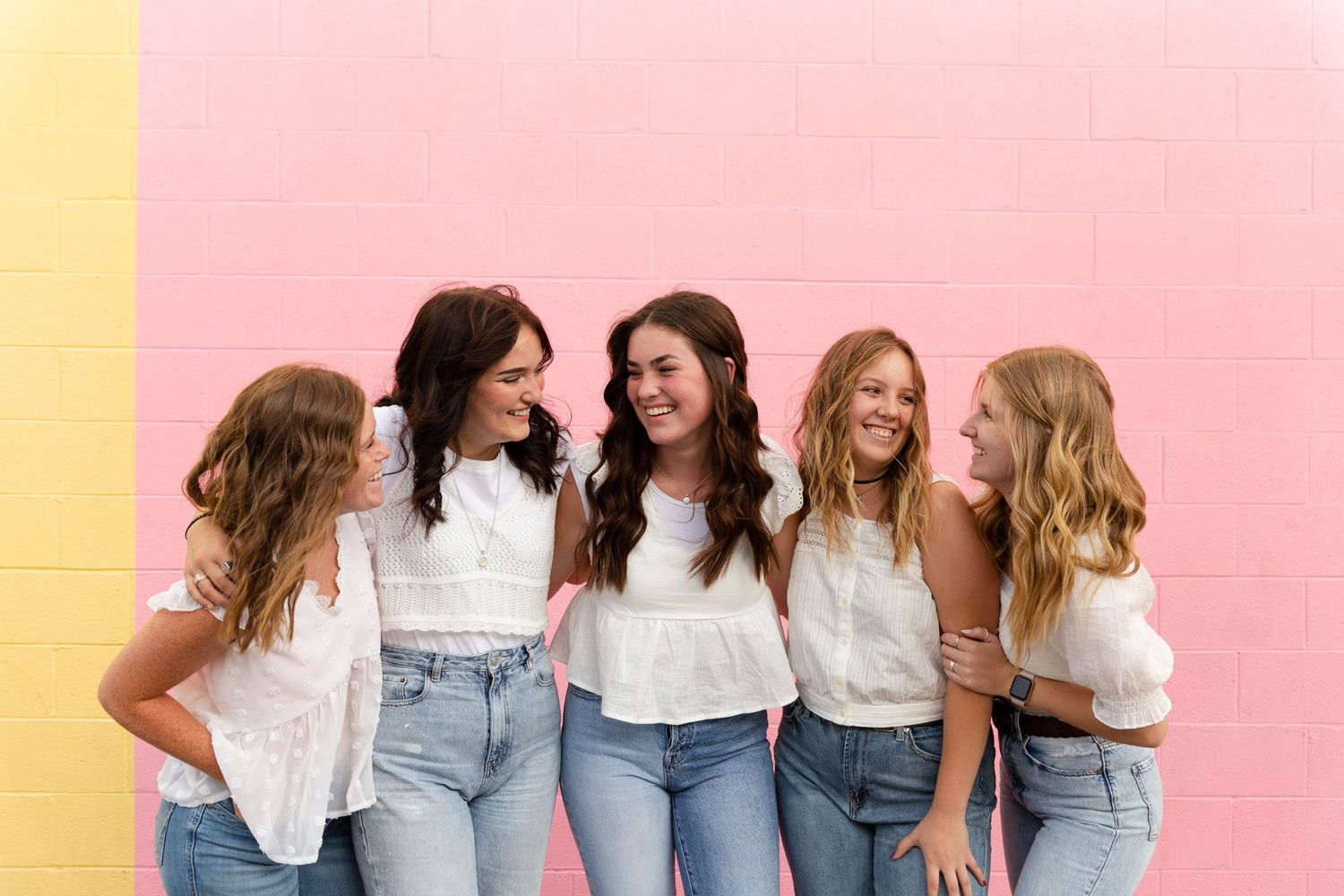 5 girls laughing together in front of pink wall