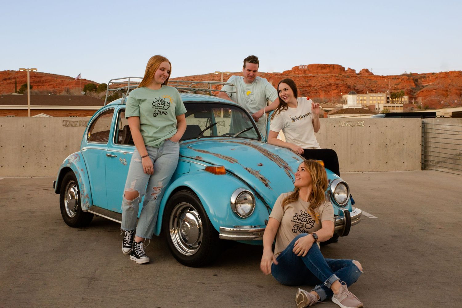 a blue slug bug car with 4 people standing around it laughing