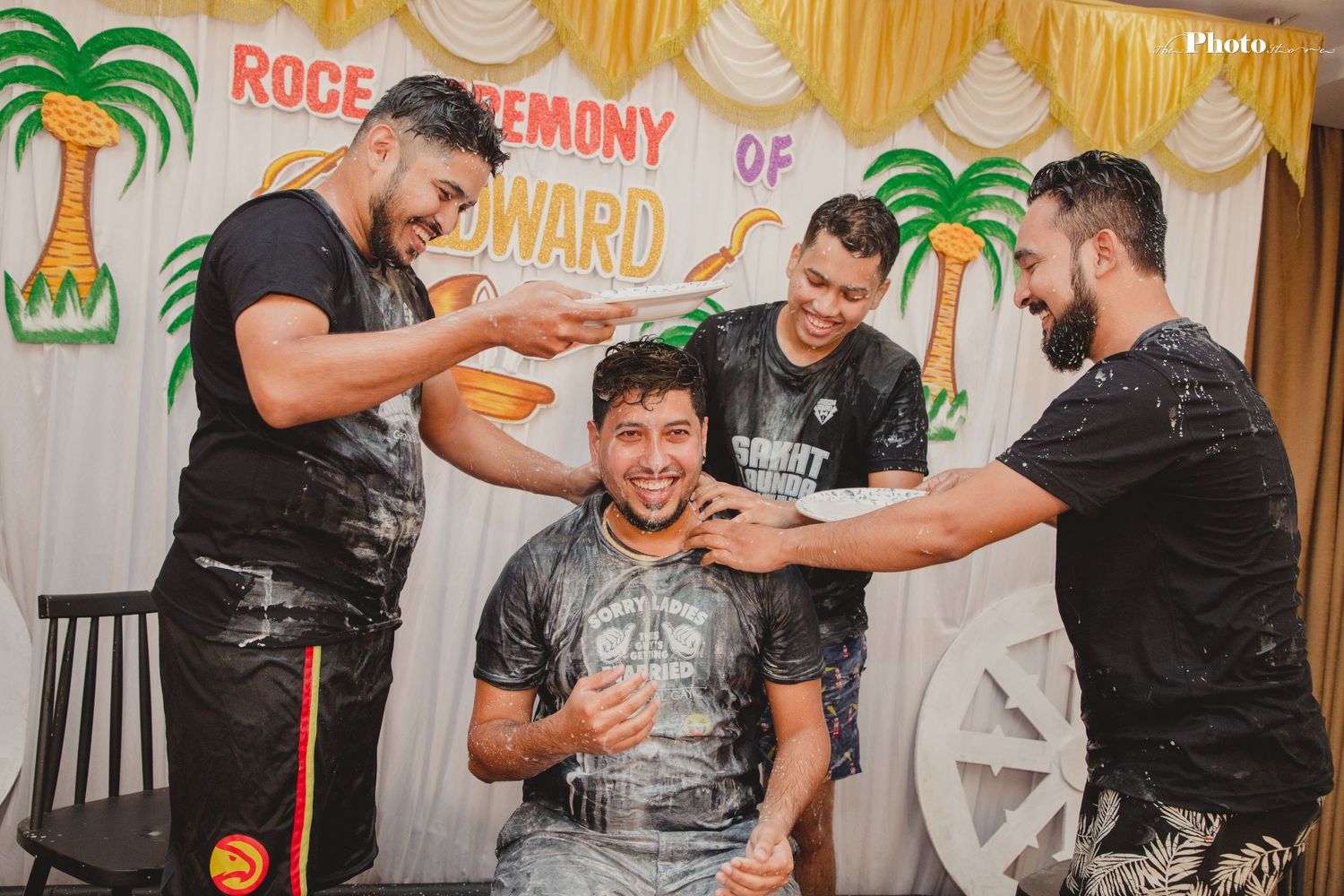People enjoying a lively indoor celebration with tropical palm tree decorations and yellow curtains in the background.