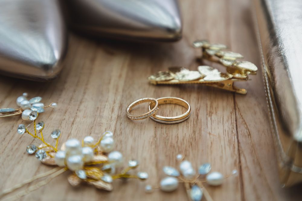 Wedding rings and pearl accessories arranged on wooden surface with silver shoes.