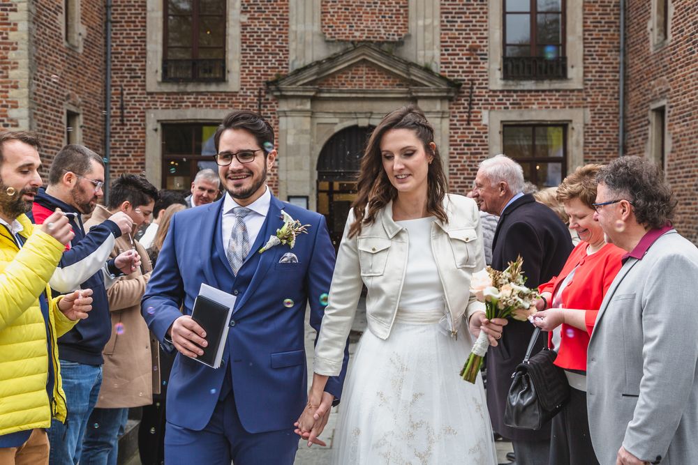 A wedding party exits a historic venue while guests celebrate with bubbles.
