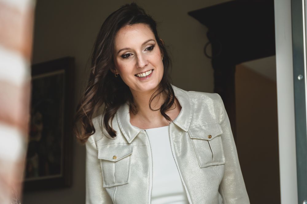 A person in a white jacket smiling warmly in an indoor setting.