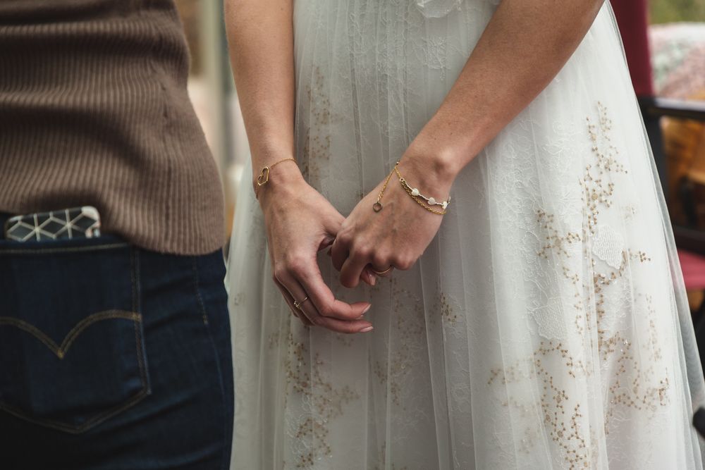 Close up of hands clasped together, one wearing jeans and the other in a white dress.