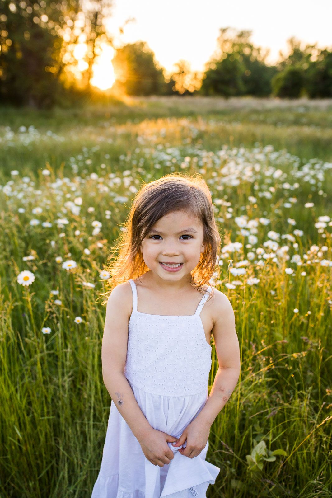 Portrait of a smiling girl in a daisy field at sunset