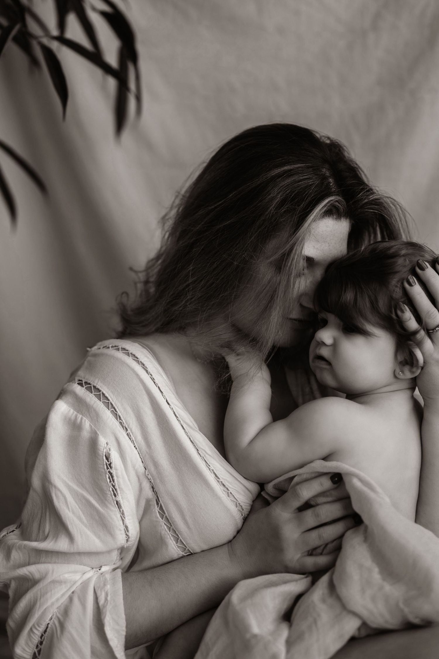 Black and white portrait showing intimate parental moment against plain backdrop.