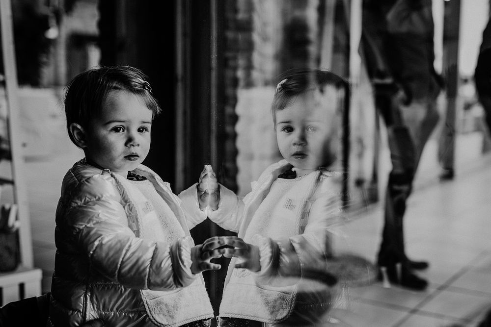 Black and white photo of a toddler boy in formal wear reflected in a glass window.