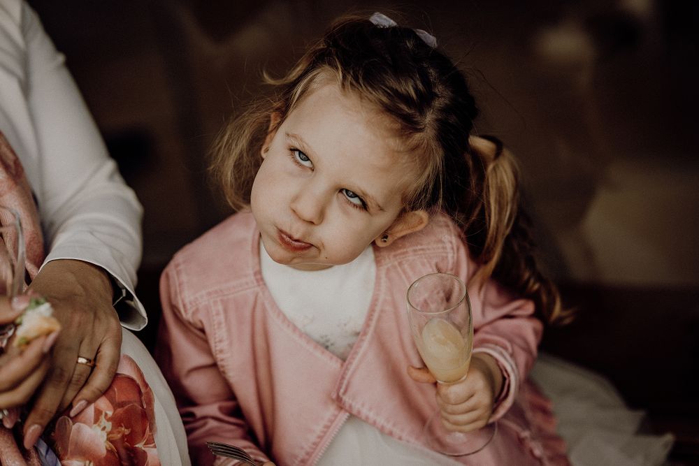 Adorable little girl in pink cardigan holding a cookie at a wedding reception.