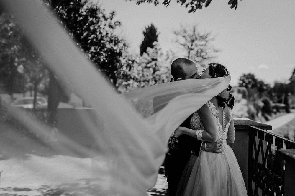 Black and white photo of bride and groom kissing with veil flowing in the wind.