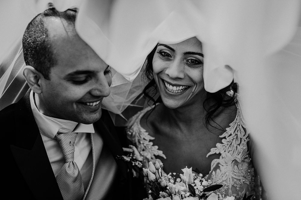 Black and white close-up of joyful bride and groom smiling together under wedding veil.