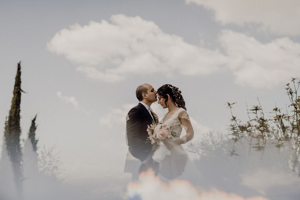Bride and groom share romantic kiss outdoors with dreamy double exposure sky backdrop.