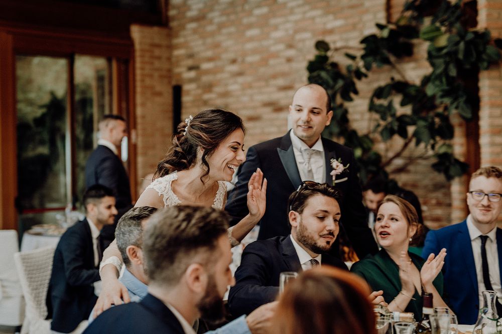 Bride and groom greet smiling wedding guests at elegant indoor reception dinner table.