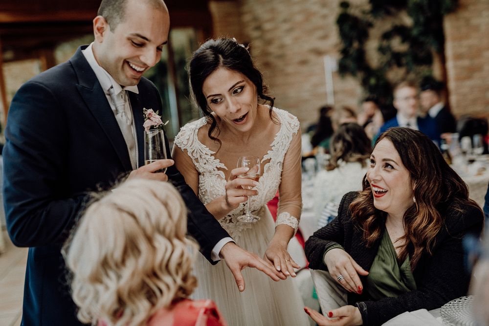 Bride and groom interact warmly with smiling guests at wedding reception dinner table.
