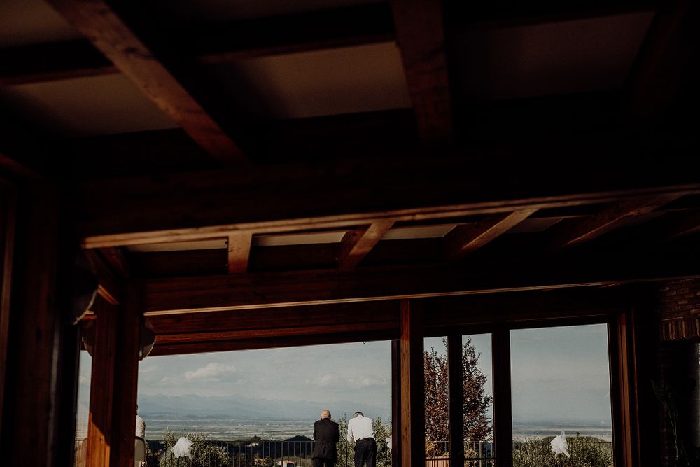 Rustic wooden ceiling frames a scenic countryside view through large glass doors at a wedding venue.