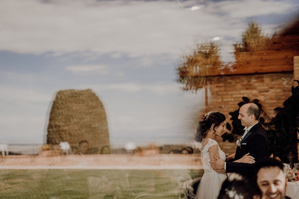 Bride and groom exchange vows outdoors near a rustic stone wall with a scenic landscape backdrop.