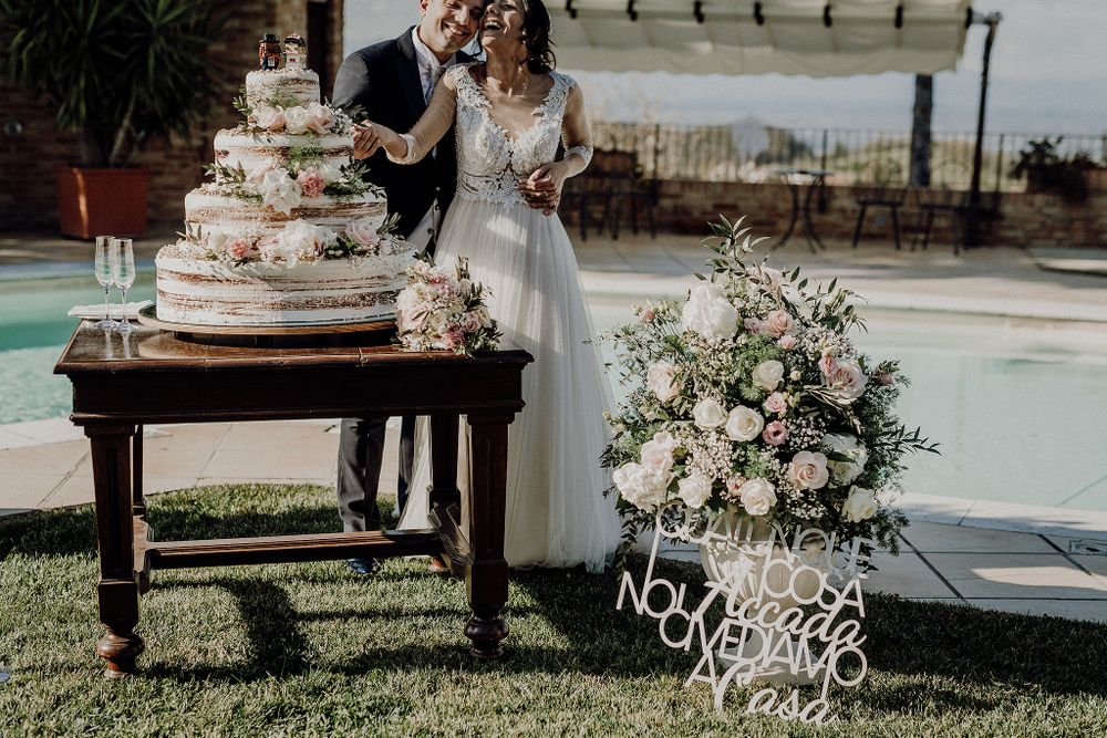 Newlyweds cut a tiered naked wedding cake beside an elegant floral arrangement near a garden pool.