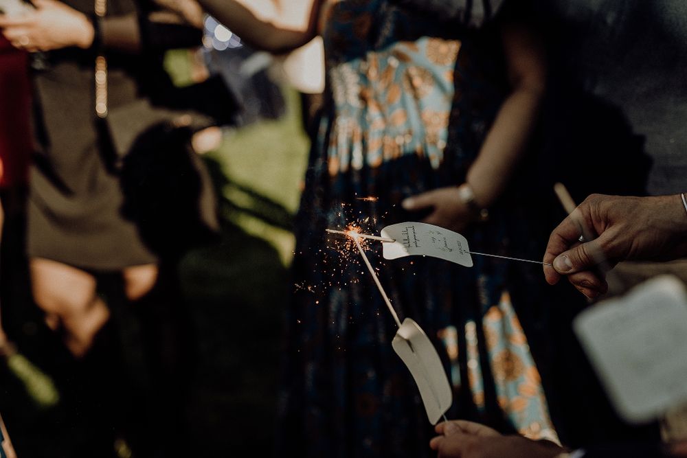 Wedding guest lights a sparkler during an outdoor celebration, creating a shower of golden sparks.