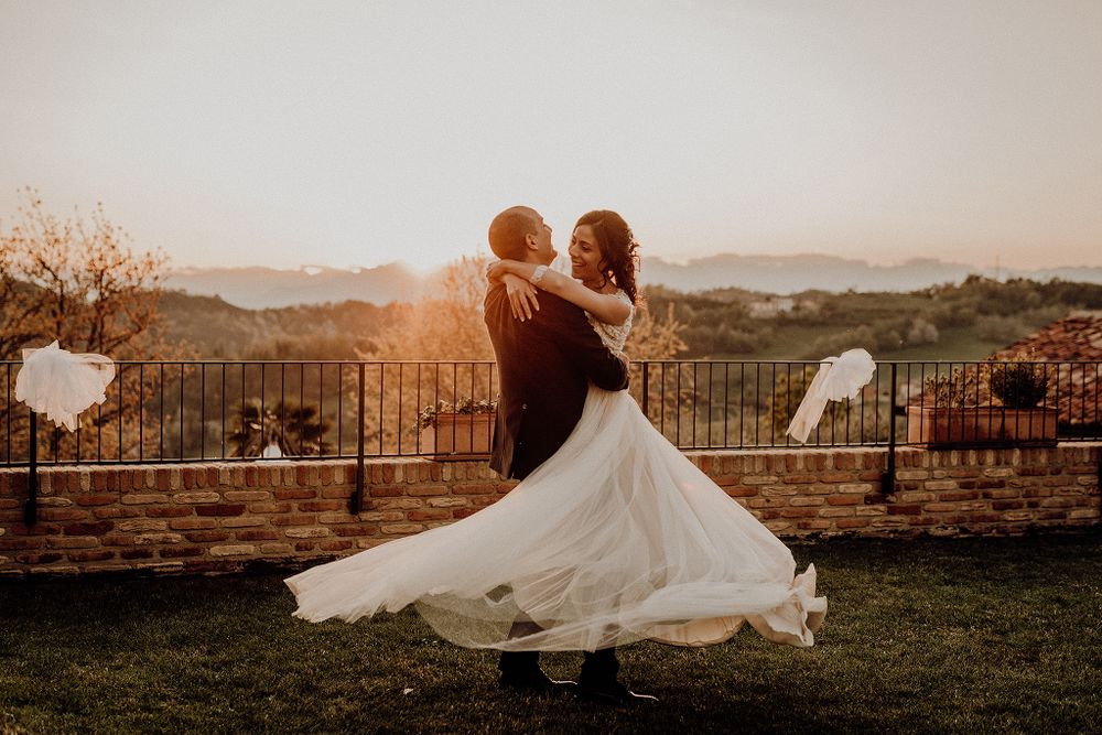 Groom twirling bride in flowing white dress at golden hour with mountain backdrop.