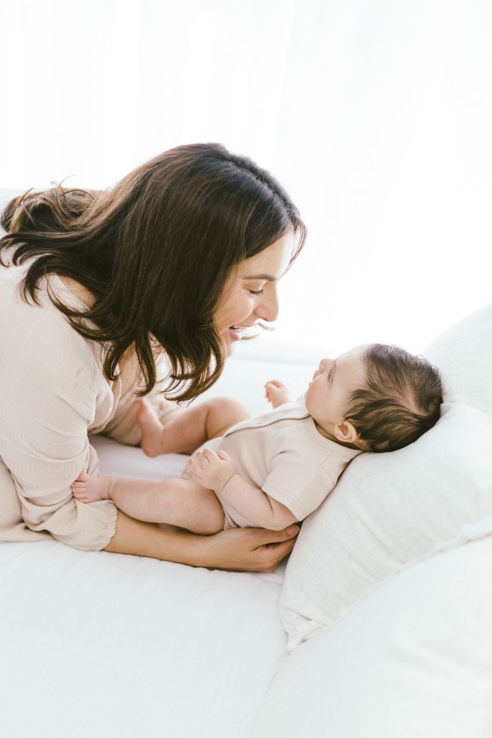 Parent and baby share intimate bonding moment while lying on white bedding.