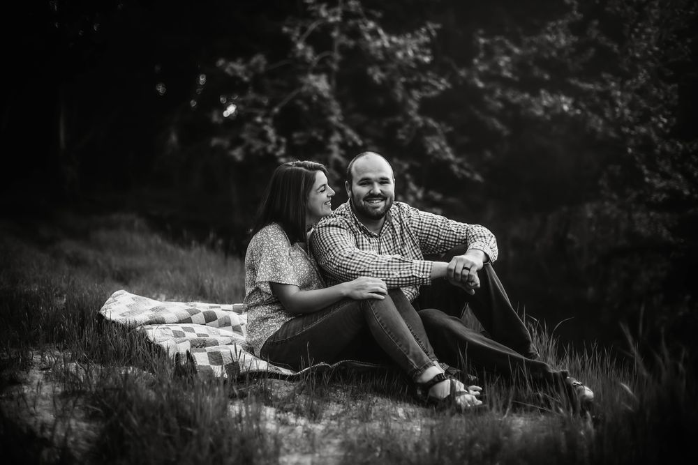 A couple relaxes on a blanket during a black and white outdoor photoshoot.