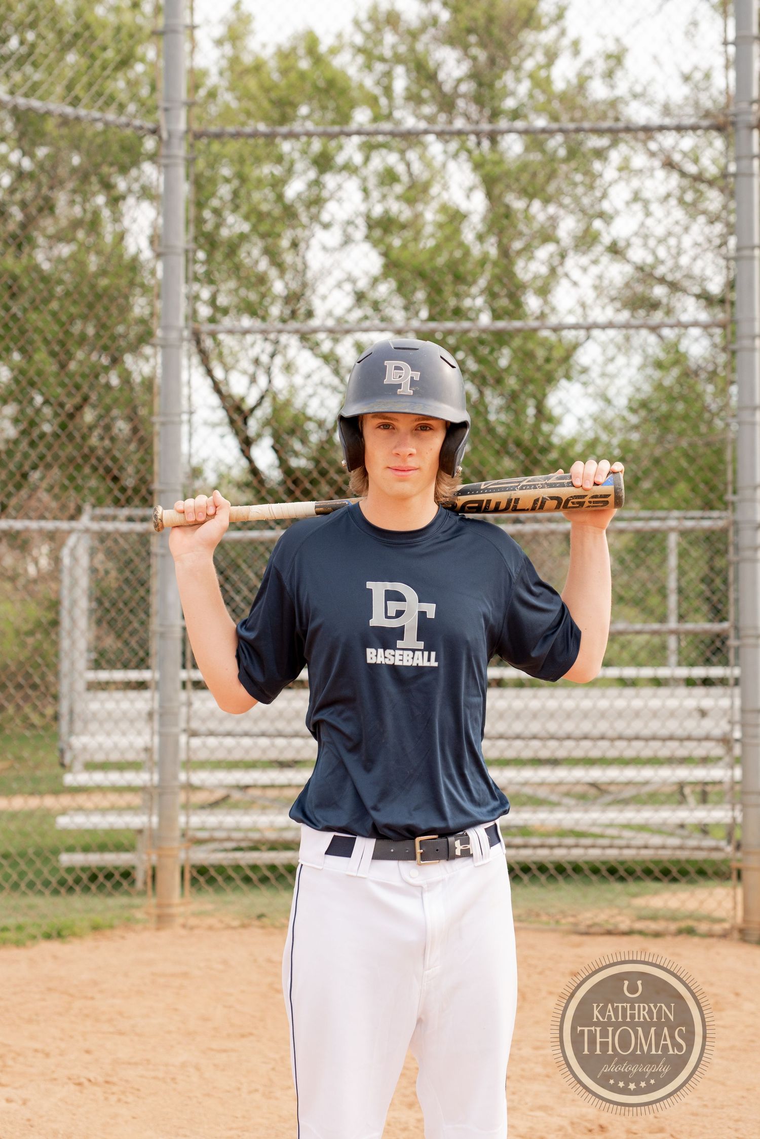 Baseball player in navy jersey holds bat over shoulders on baseball field.