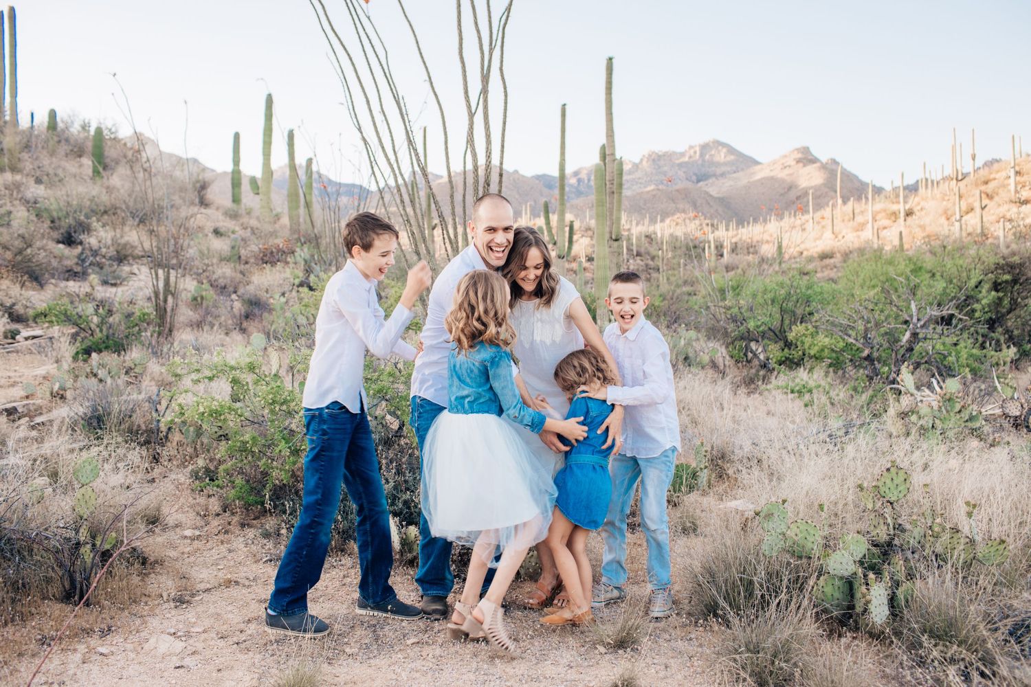 Tucson family photography of parents and children walking through the desert with saguaros and mountains in the background.