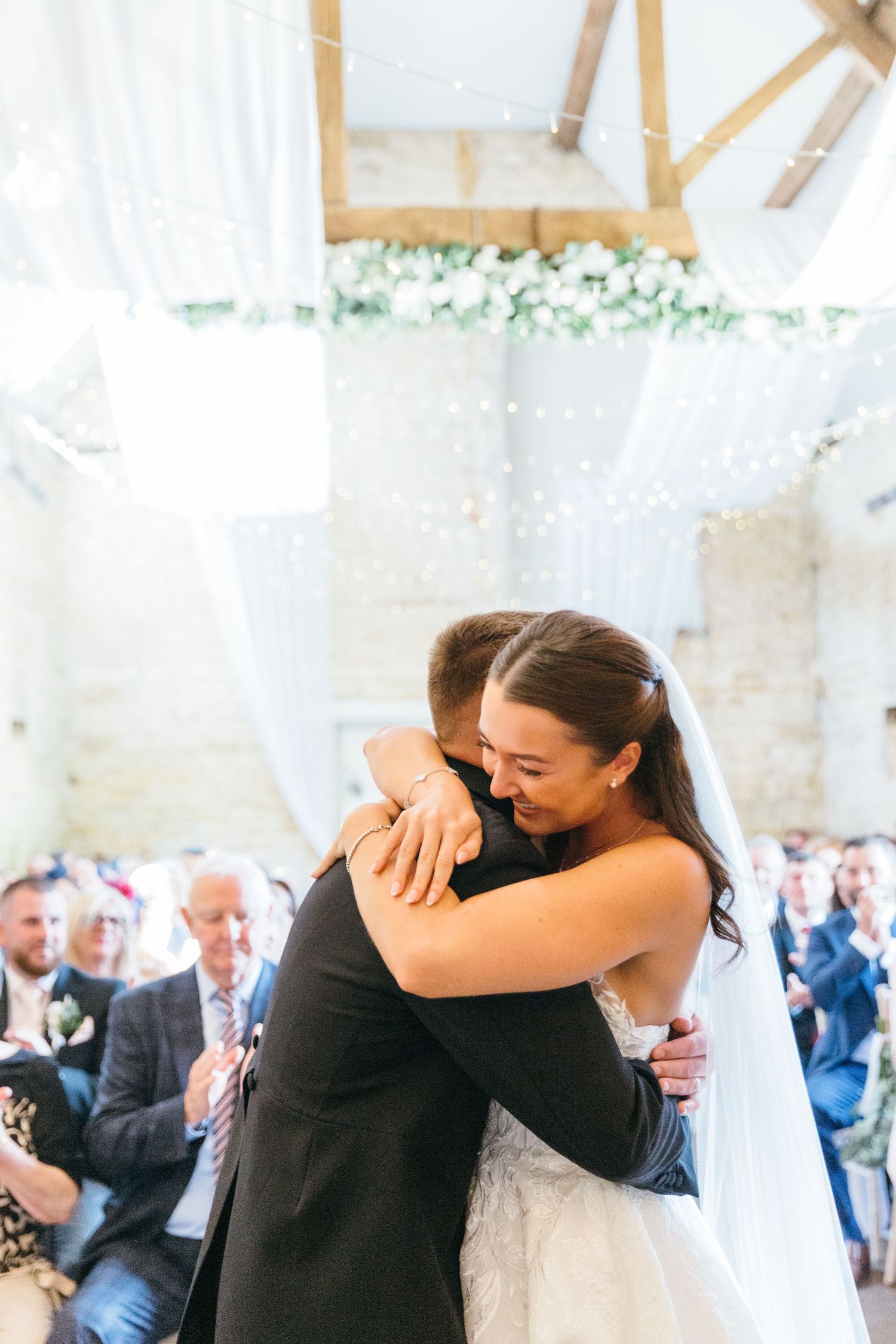 An emotional embrace during a wedding ceremony under a decorated tent with guests looking on.