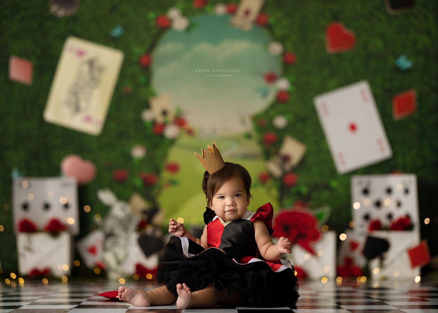 Baby in Alice in Wonderland themed photo with playing cards and whimsical decorations.