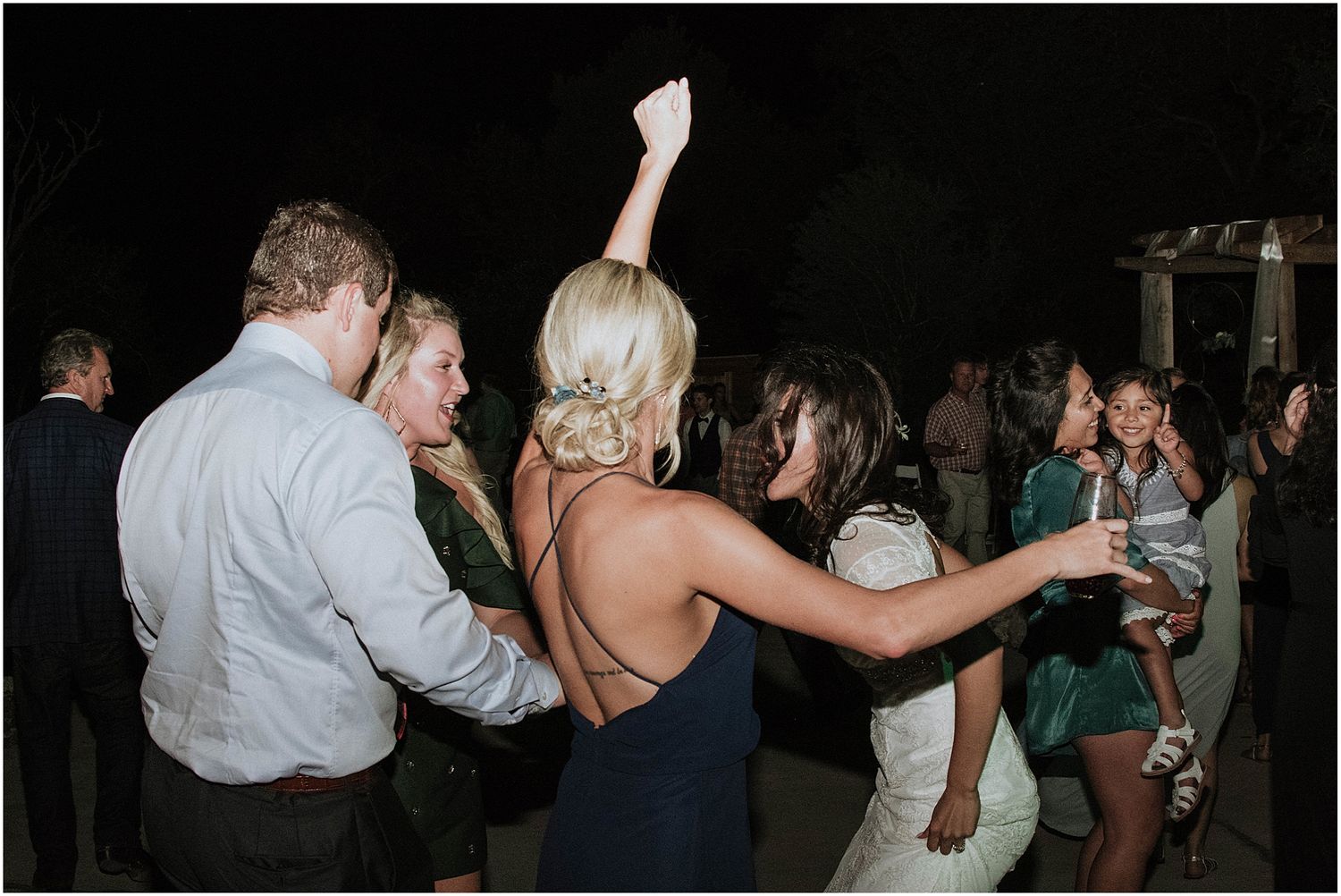 Wedding reception dance party with guests enjoying themselves under evening lighting.