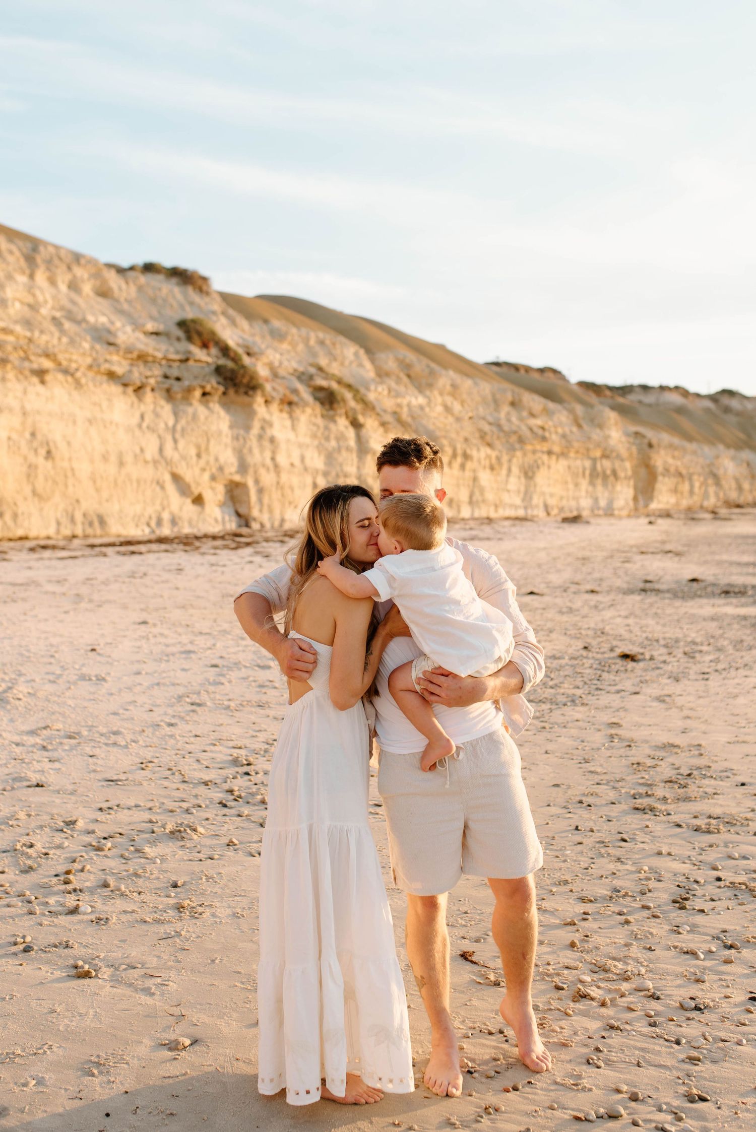 Family embracing on beach with dramatic coastal cliffs during golden hour.