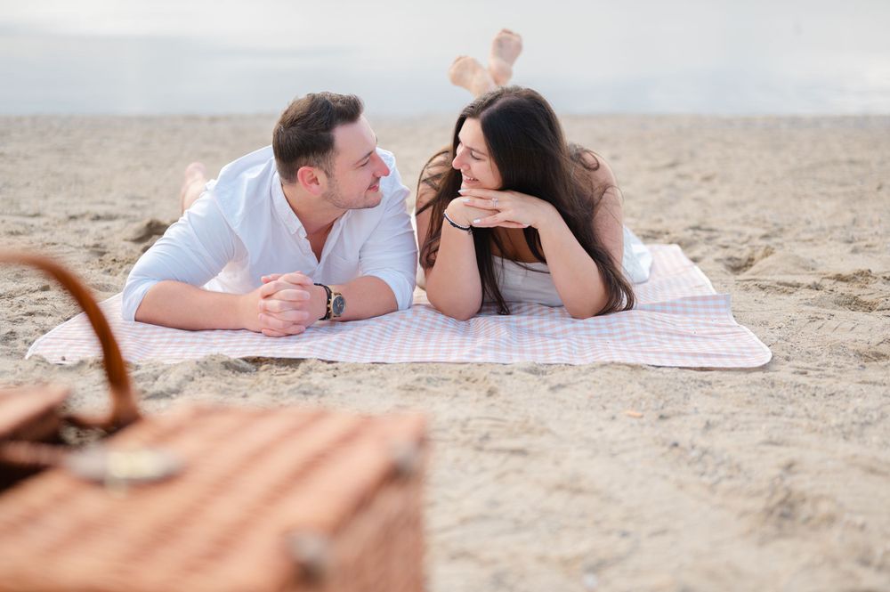 Couple enjoying a romantic picnic date on a sandy beach with a wicker basket.