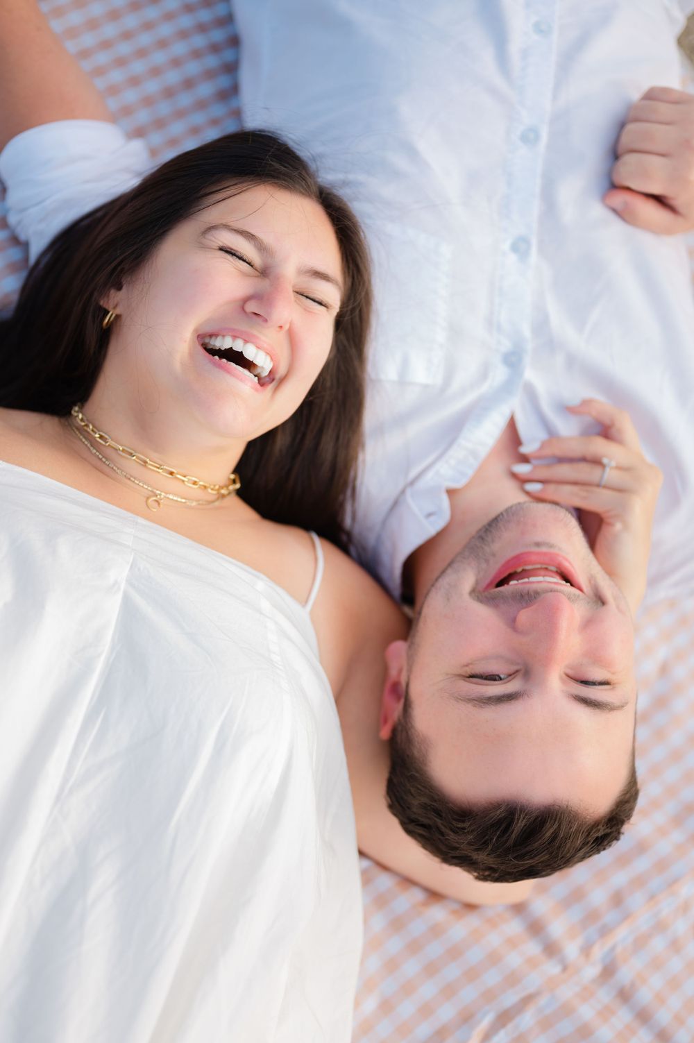 A joyful couple wearing white clothing laying down together and laughing.