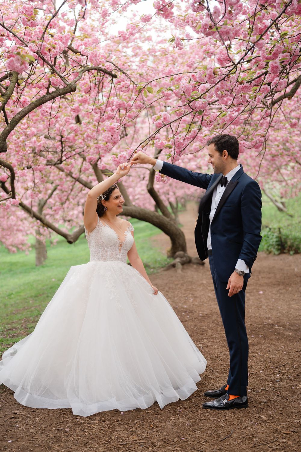 A couple dancing under blooming cherry blossom trees in wedding attire.