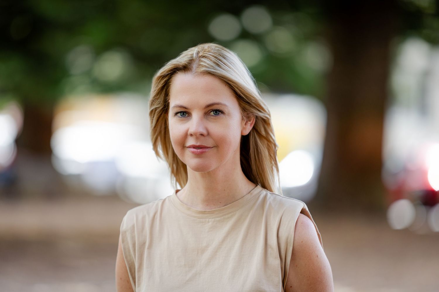 Casual outdoor portrait of someone in a beige sleeveless top with trees in background.