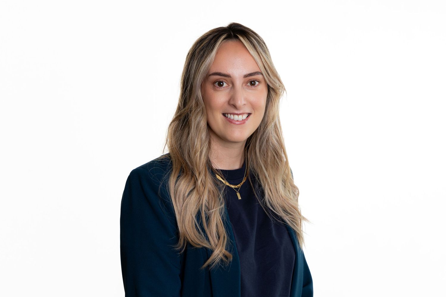 Professional portrait of a person with long blonde hair wearing a navy sweater.